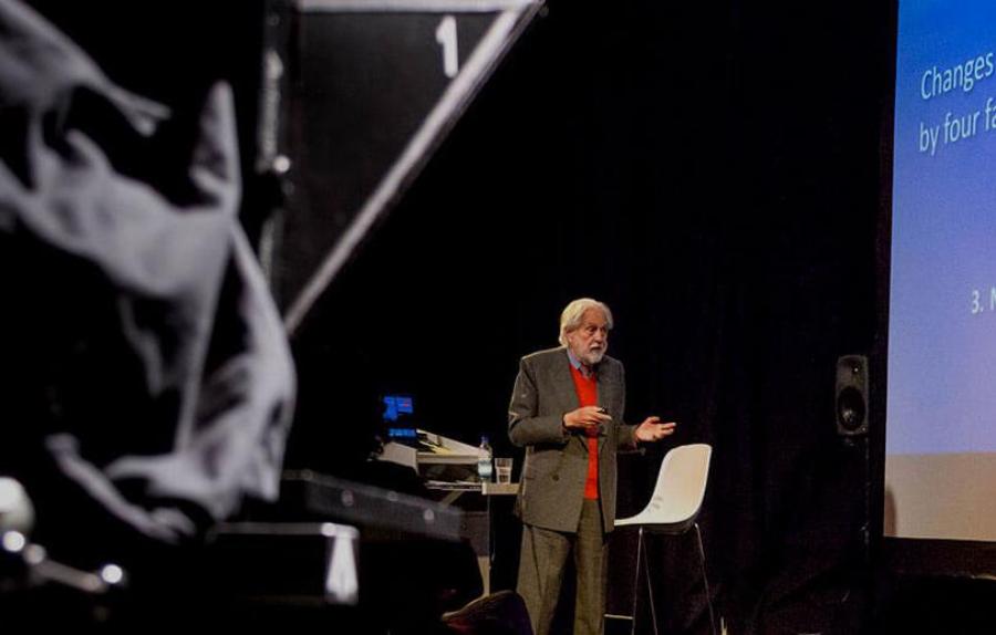Lord David Puttnam delivers talk on stage, with filming equipment in foreground