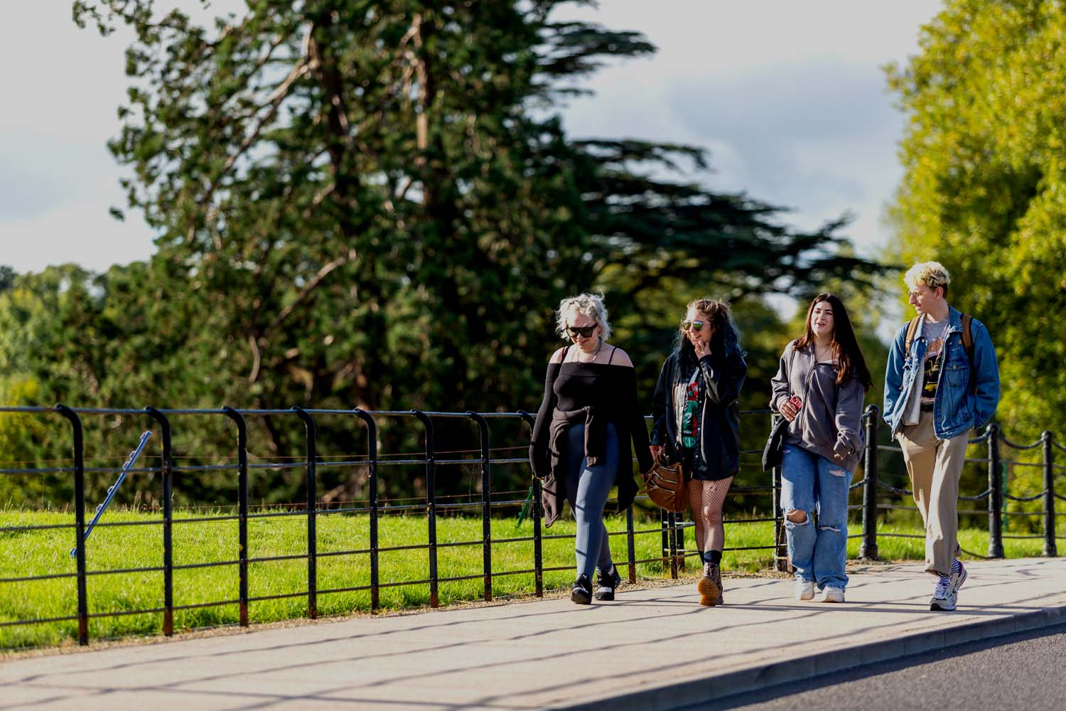 A group of four smiling students walk along a path on Newton Park campus