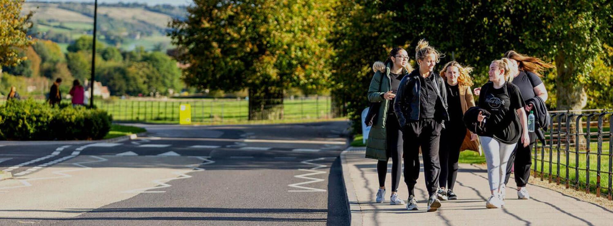 A group of students walk on the pavement through Bath Spa Newton Park campus
