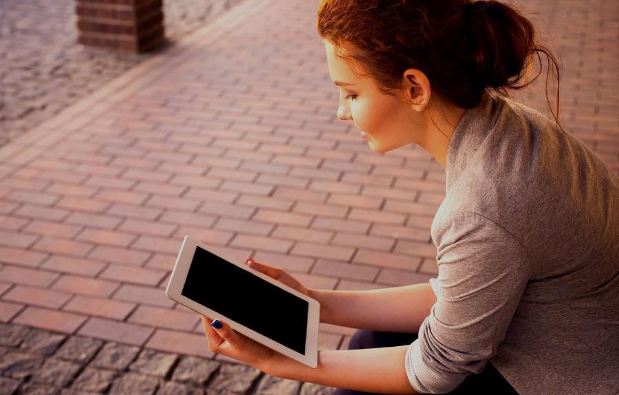 A woman with a blue painted nails holding and reading on an iPad tablet beside a pavement