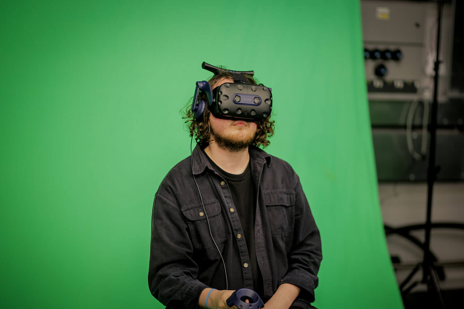 Student sitting against a green screen while wearing a virtual reality headset