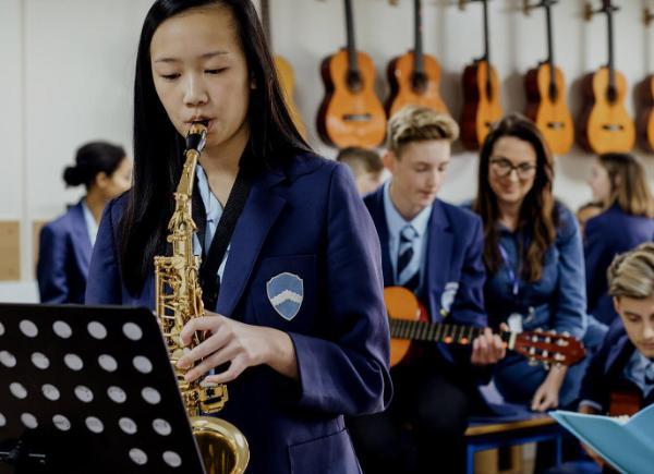 Teen student playing the saxophone in school music lesson.