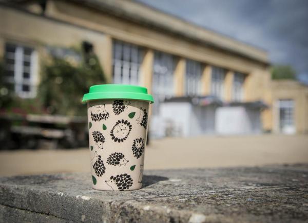A reusable coffee cup with a cute hedgehog motif sitting on a table outside the Refectory.