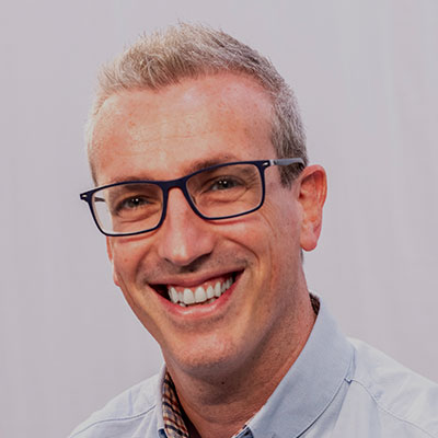 A smiling man with short grey hair and glasses