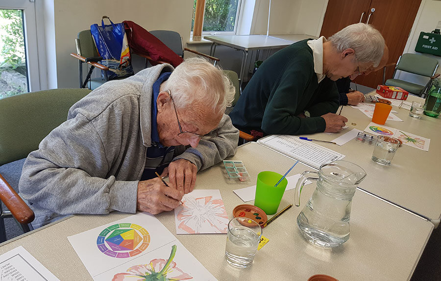 Two elderly men sit at a table painting with watercolour