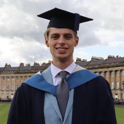 A student wearing Bath Spa University graduation robes stands outside the Royal Crescent