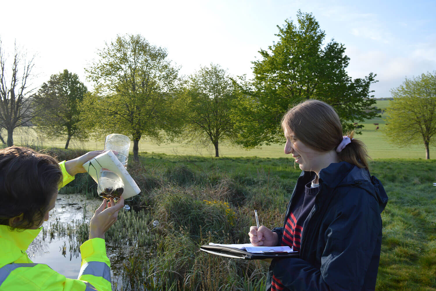 Student recording notes while an ecology consultant examines a sample