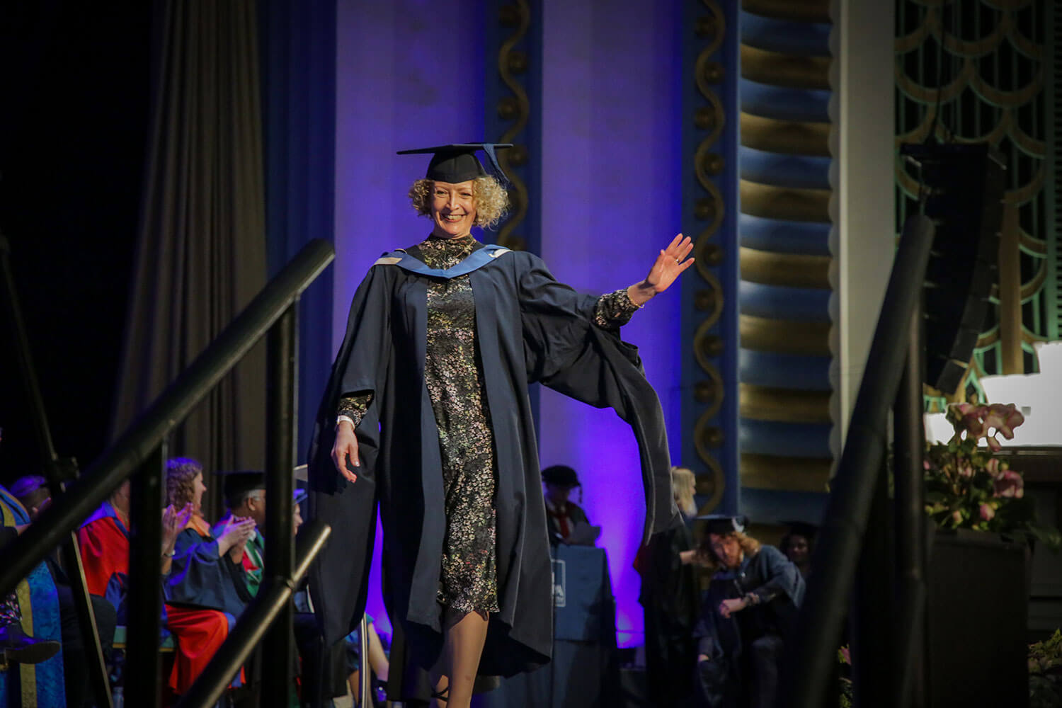 Graduand walks confidently across the stage, waving at the crowd
