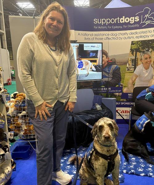 A woman stands, smiling, with her dog by her side