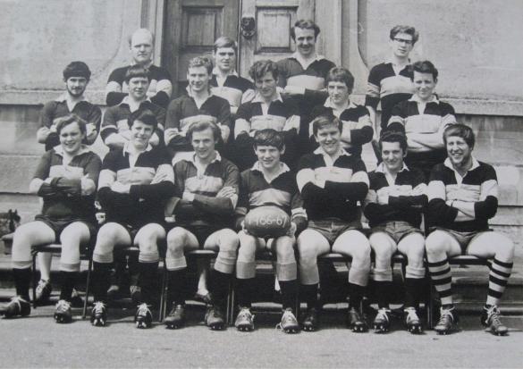 A black and white photo of a male rugby team, standing and sitting outside Main House