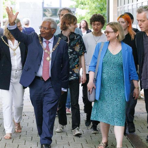 A man and a woman walk together, the man has his hand raised
