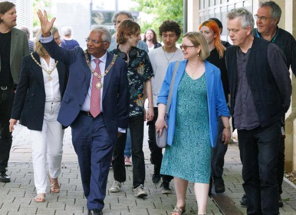 A man and a woman walk together, the man has his hand raised
