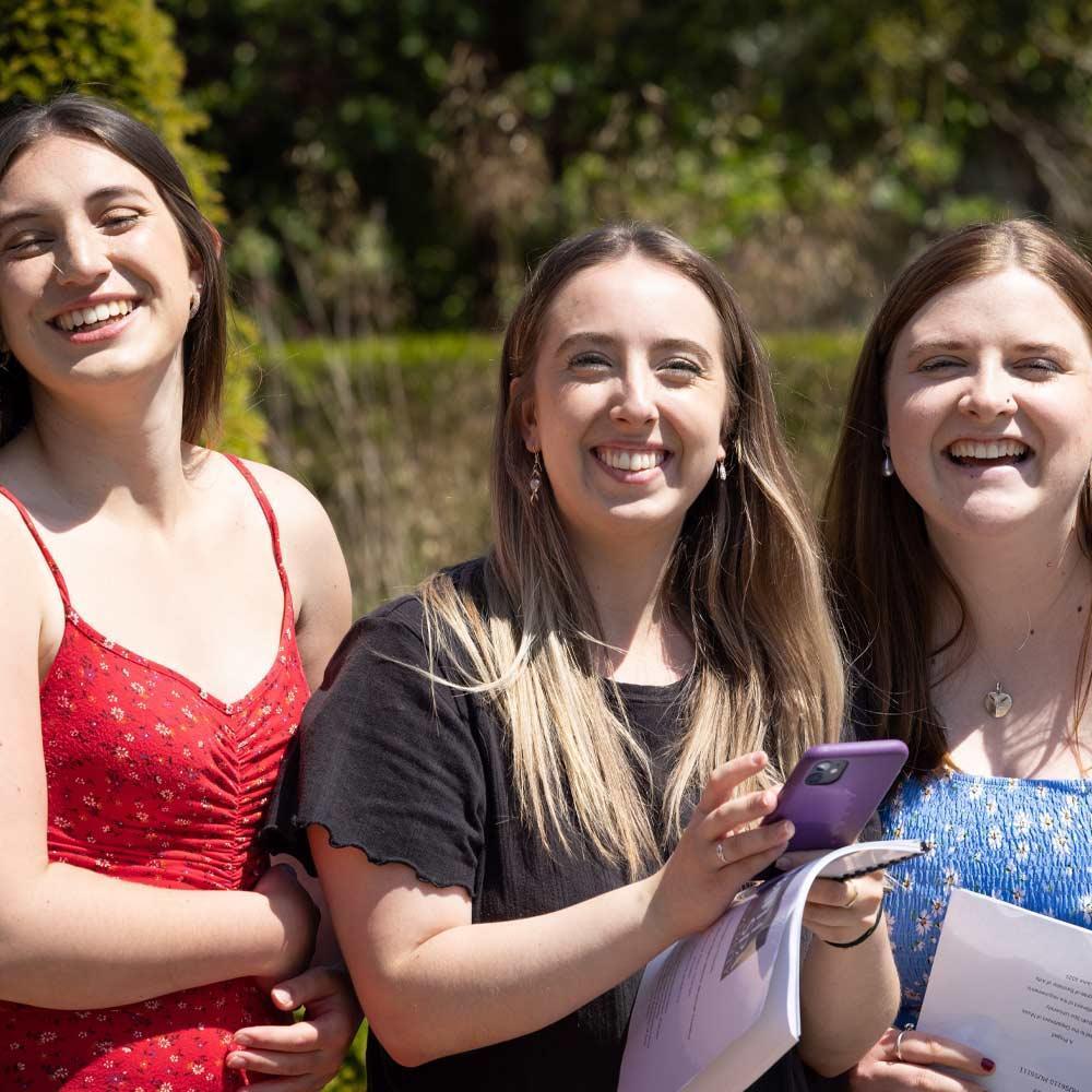 Three people with long hair smiling in front of a hedge