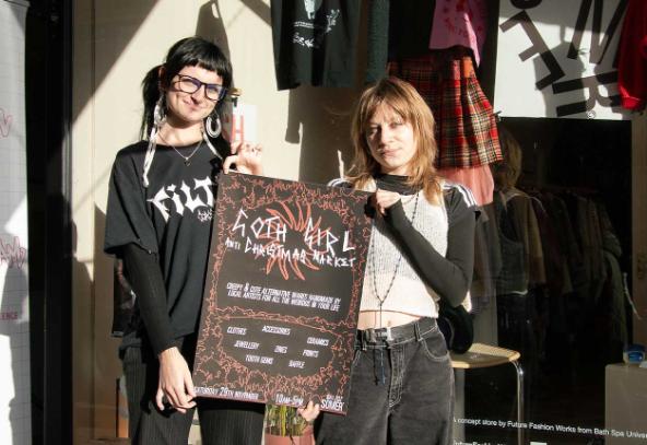 Two girls stand in front of the Somer store window, holding a sign