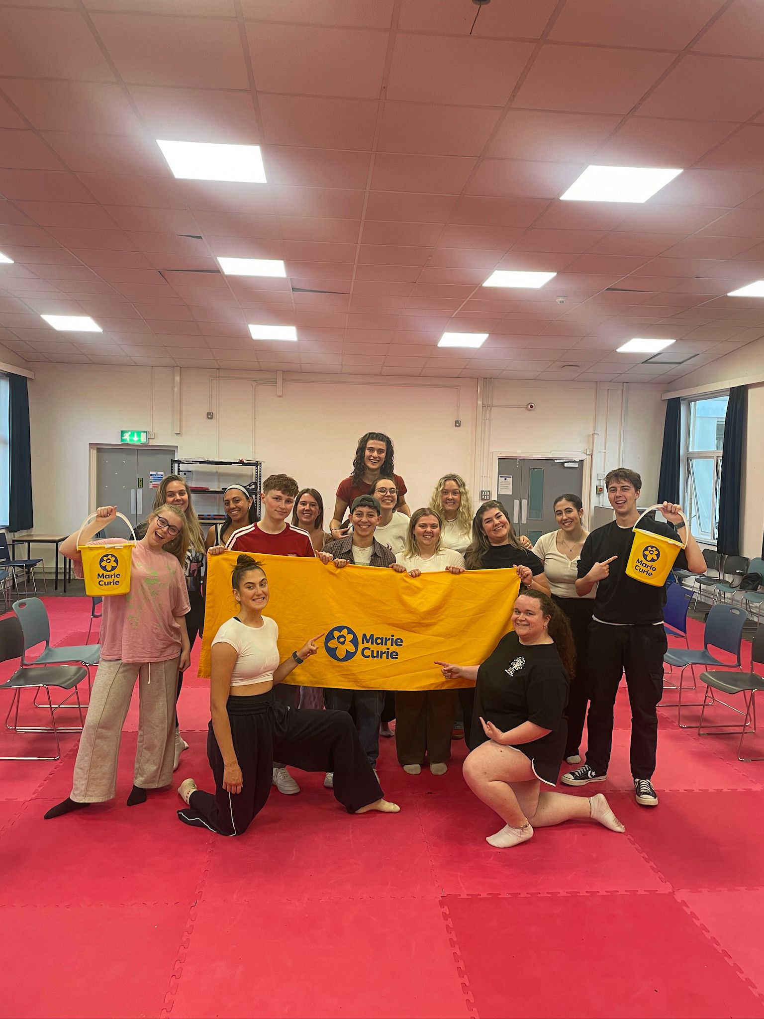 Members of the musical theatre society group together and hold yellow Marie Curie banner and pots