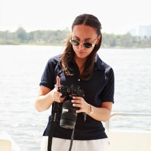 Brown haired girl with sunglasses on, stood looking down at camera on a boat,