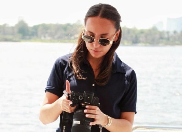 Brown haired girl with sunglasses on, stood looking down at camera on a boat,