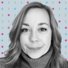 A woman with curled hair in a side part smiles at the camera against a patterned background.