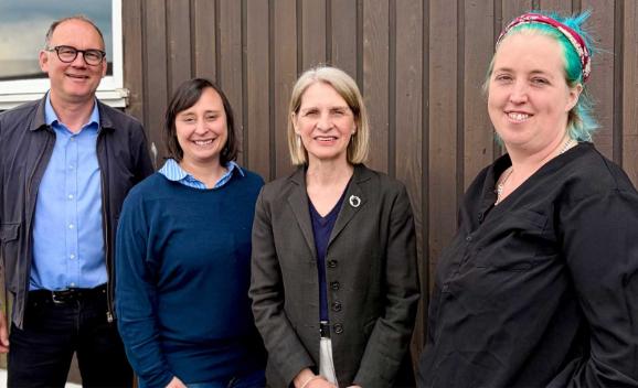 A group of people stand against a wall for a smiling photo