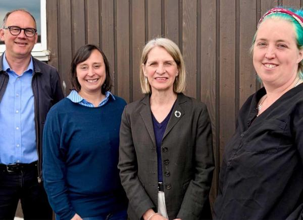 A group of people stand against a wall for a smiling photo