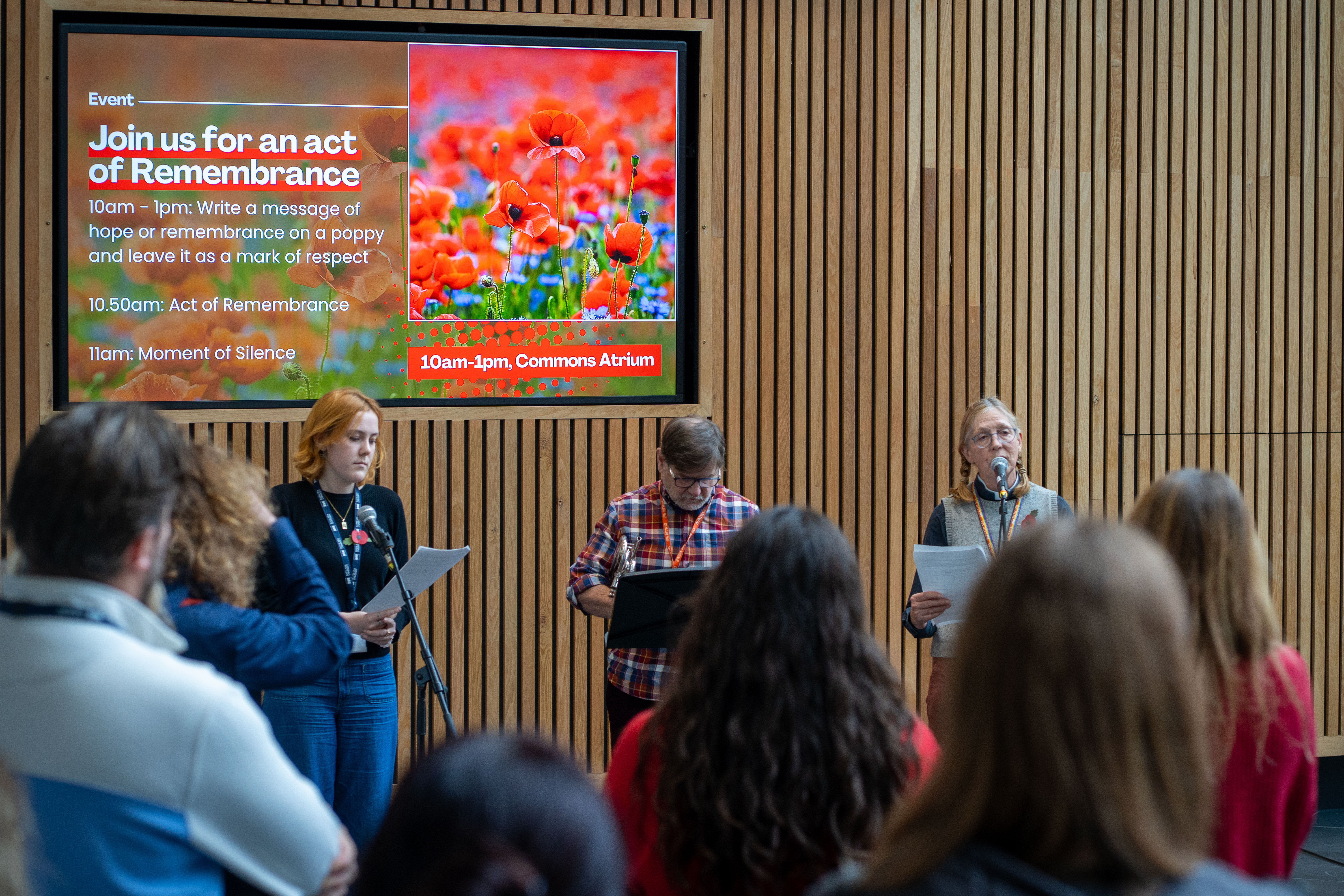 Three people stood by microphones, next to a poppy display