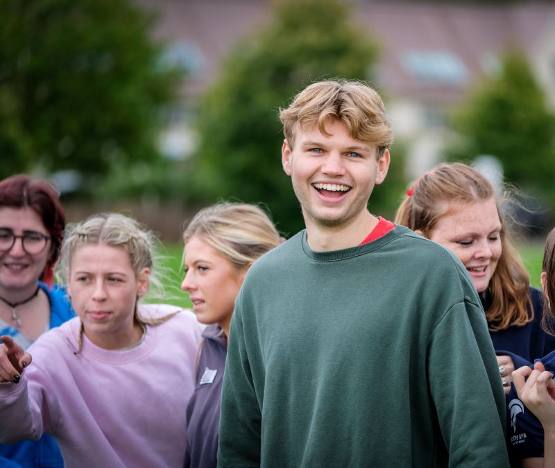A student smiling at the camera with a few students around them in the background
