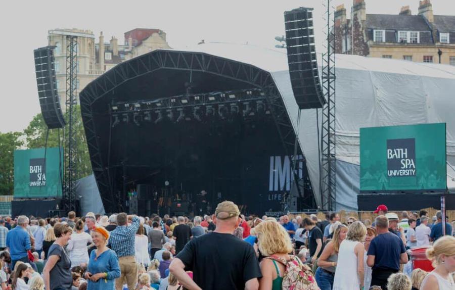 A crowd stood in front of a large stage with screens either side displaying the Bath Spa logo2