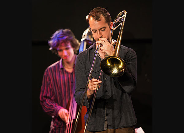 Jazz musician playing the trombone on the right with a double base player to his left in the background2