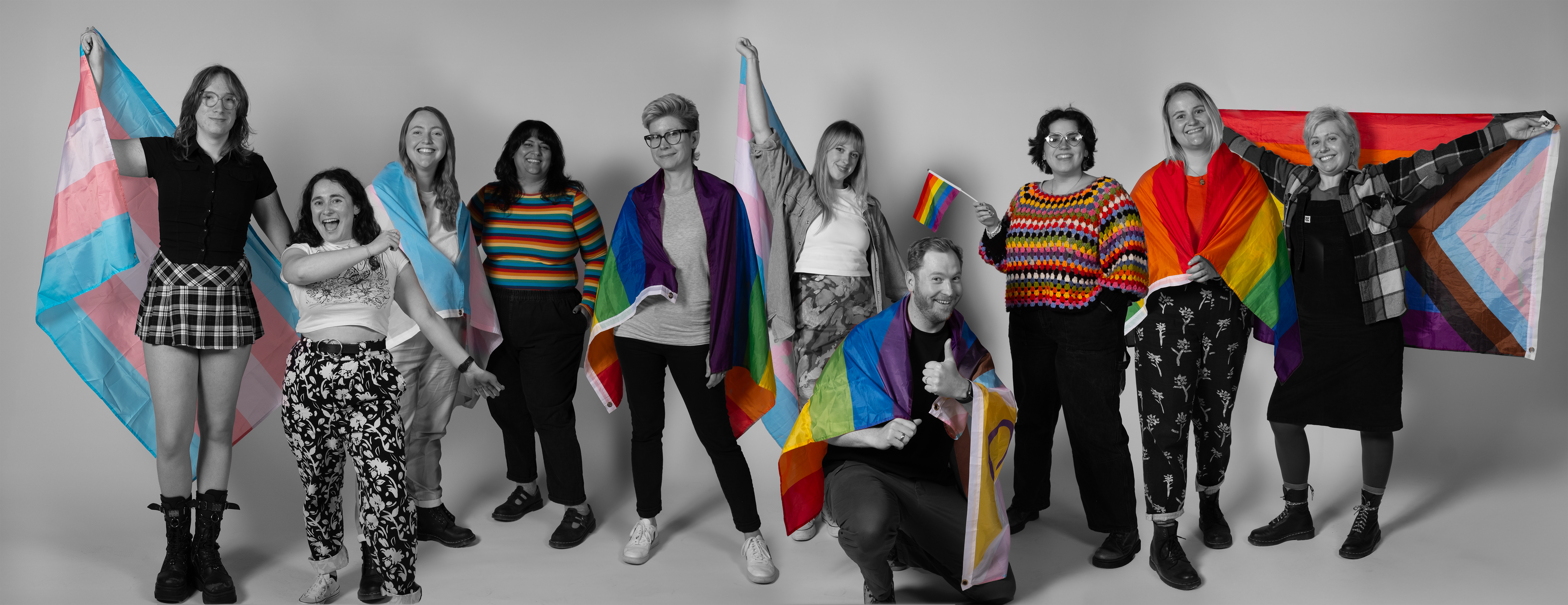 A diverse group of people draped in colourful pride flags
