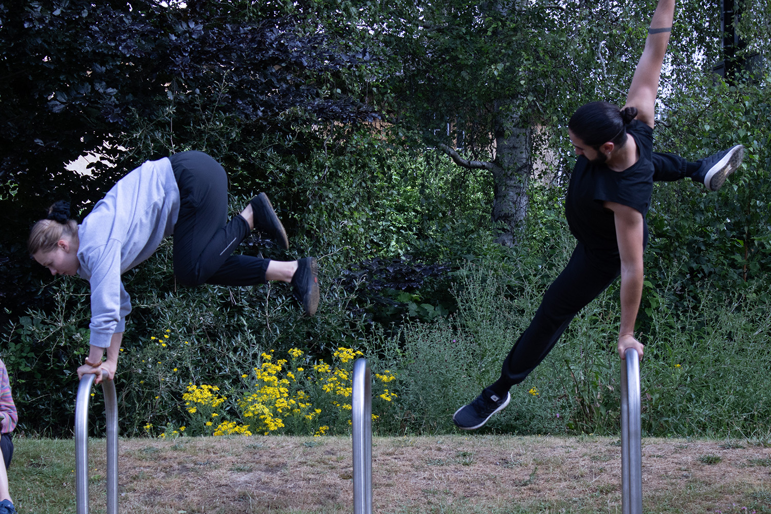 Two performers vault over metal bike racks.