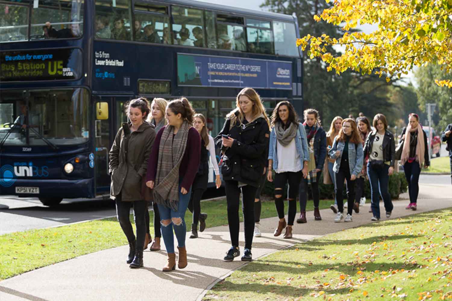 Group of young people walking on pavement alongside university bus
