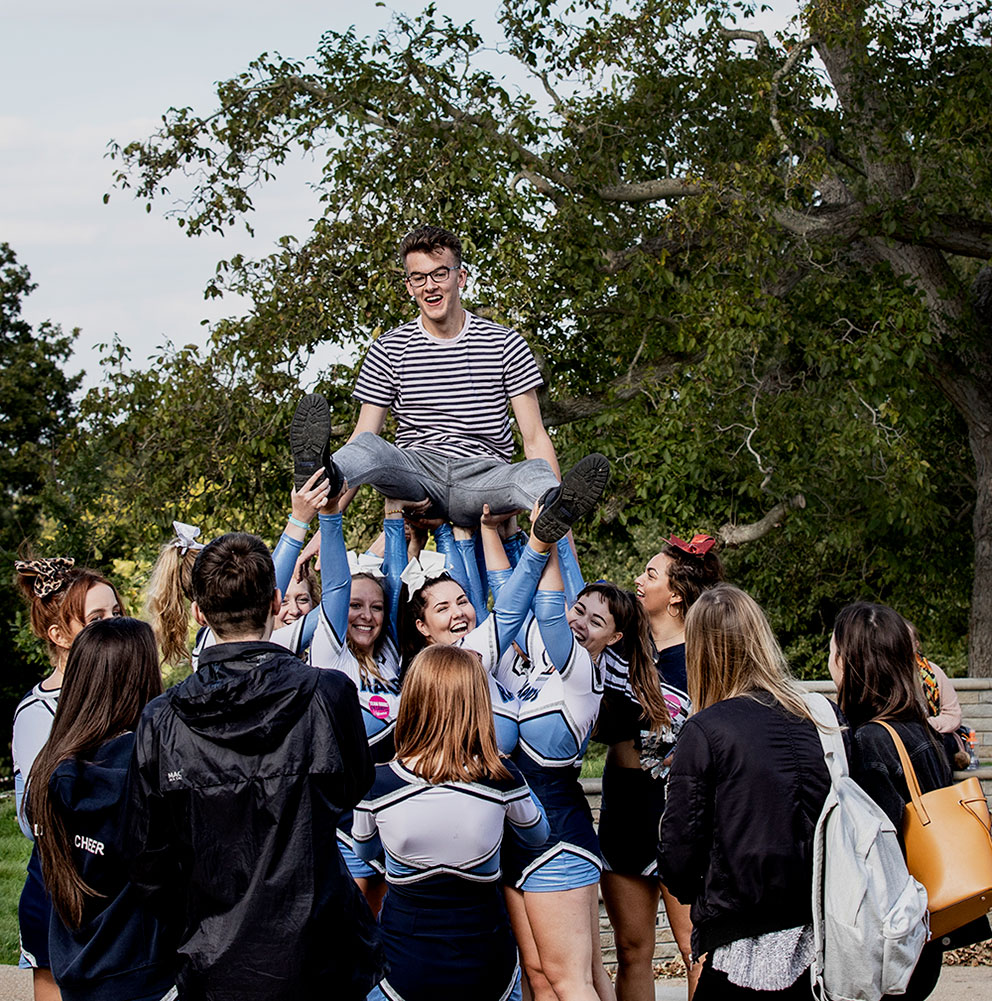 Cheer squad carrying a guy in a striped shirt