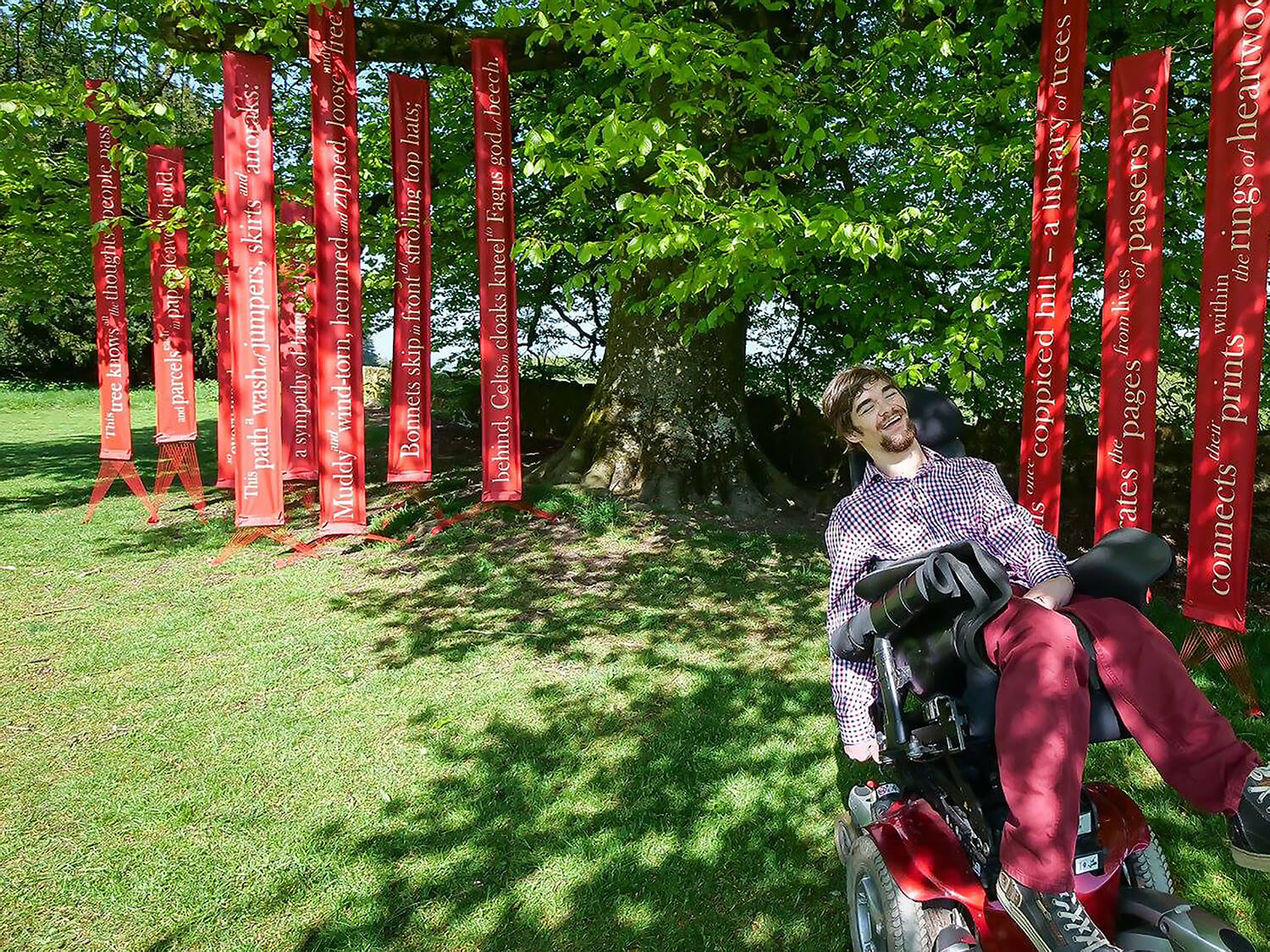 Student in wheelchair under trees and art installation