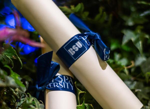 Two Bath Spa University certificate scrolls on a bed of leaves.