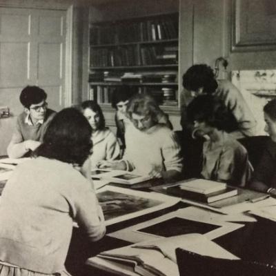 Black and white image of a group of students looking at a book 
