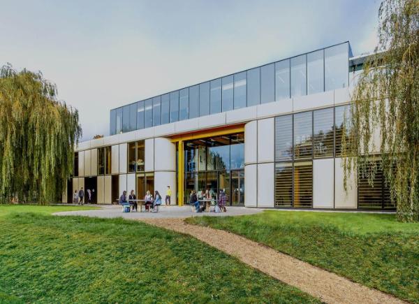 Exterior of a period factory building with modern glazing design, flanked by mature willows, with students in the outdoor seating area