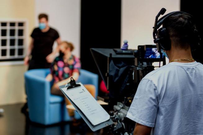 Student using a film camera to capture images of people on set