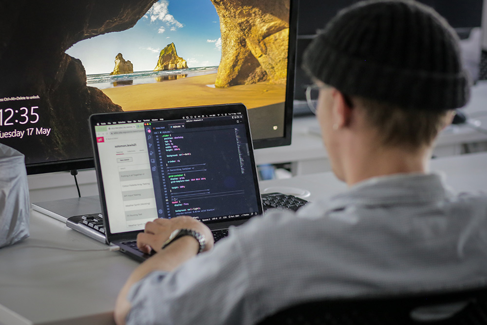 Looking over the shoulder of a student working on some code on a laptop