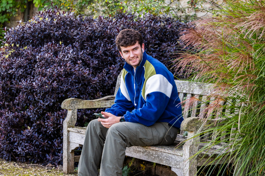 A male student sat on a park bench in a blue coat