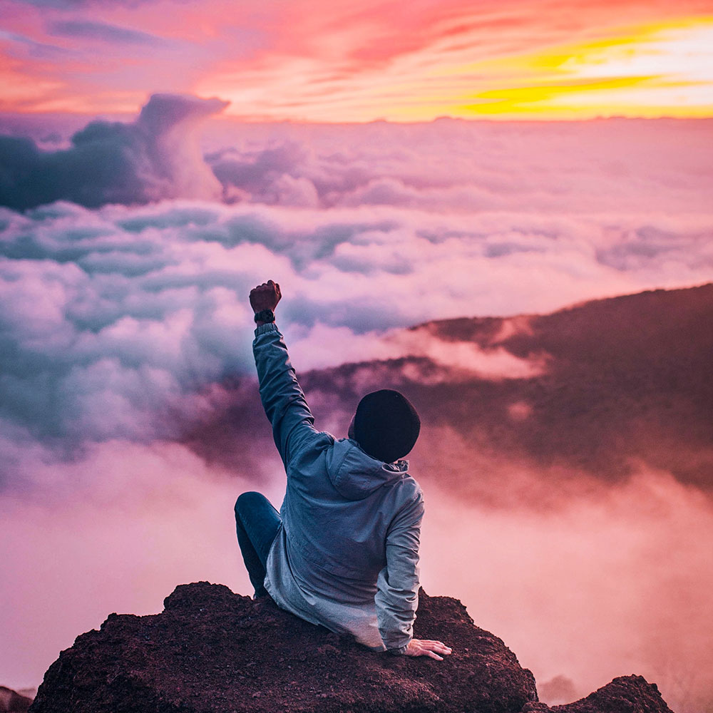 A man punching the air in celebration at the summit of a mountain