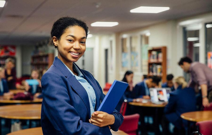 Confident school pupil holds her books in her classrom