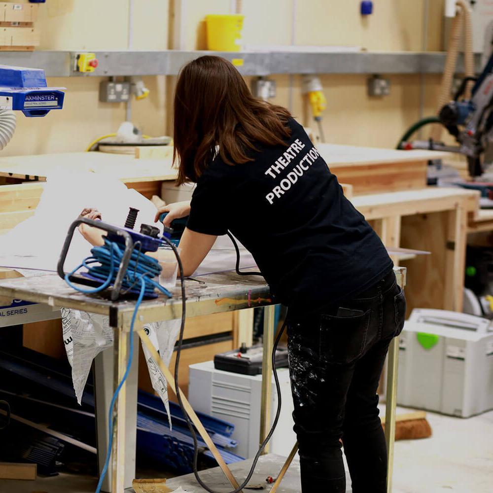 Student with 'Theatre Production' t-shirt working in carpentry studio