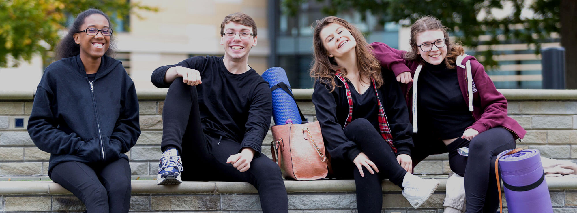 Smiling students sitting on a wall