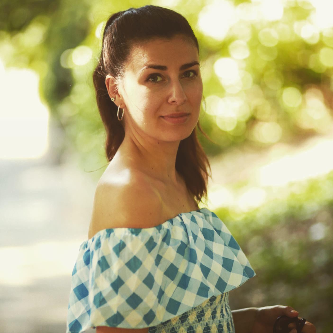 Image of a young woman with dark hair standing in a sunny forest