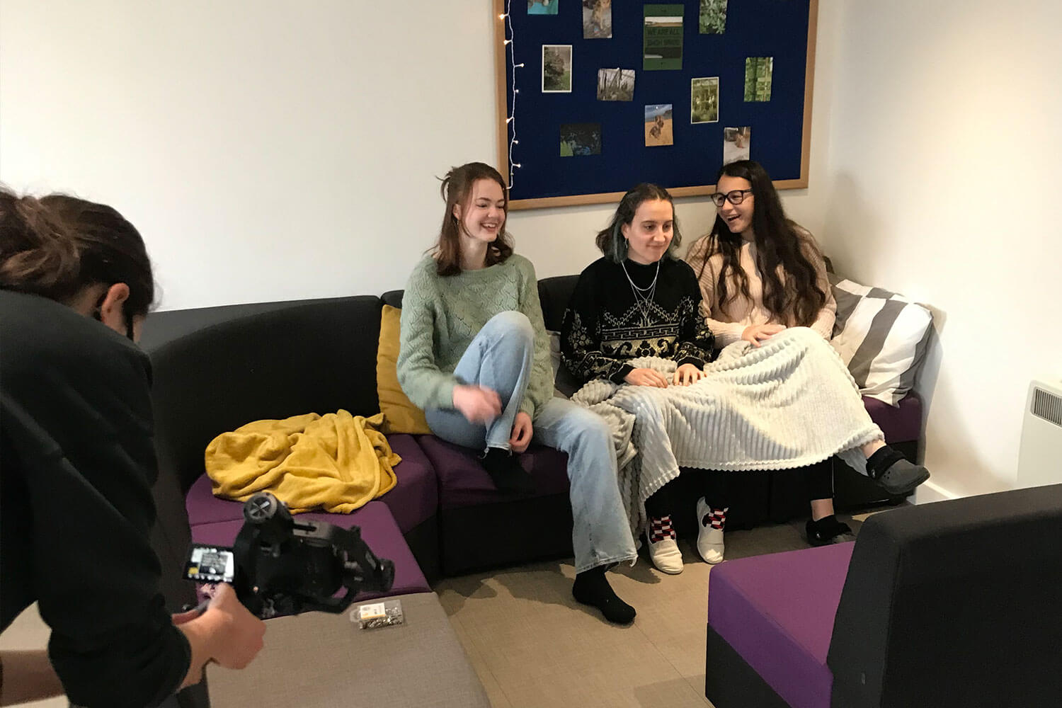 Three girls sat on a sofa being filmed