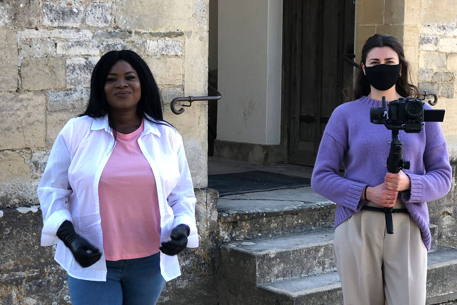 Portrait of two women, one wearing a face mask and holding a camera, the other wearing gloves