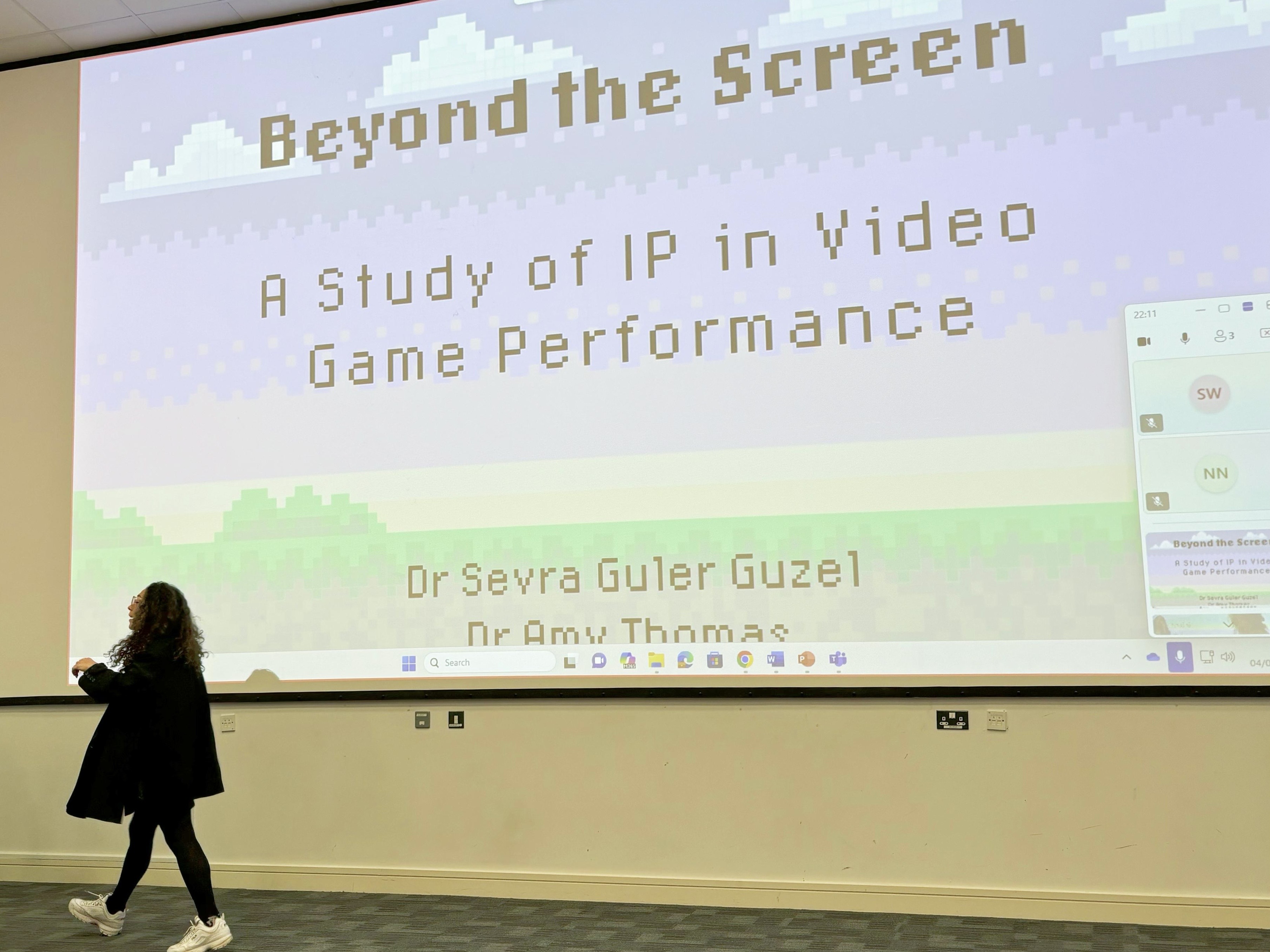 A presenter stands in front of a large screen which reads 'Beyond the Screen: A study of IP in video game performance'