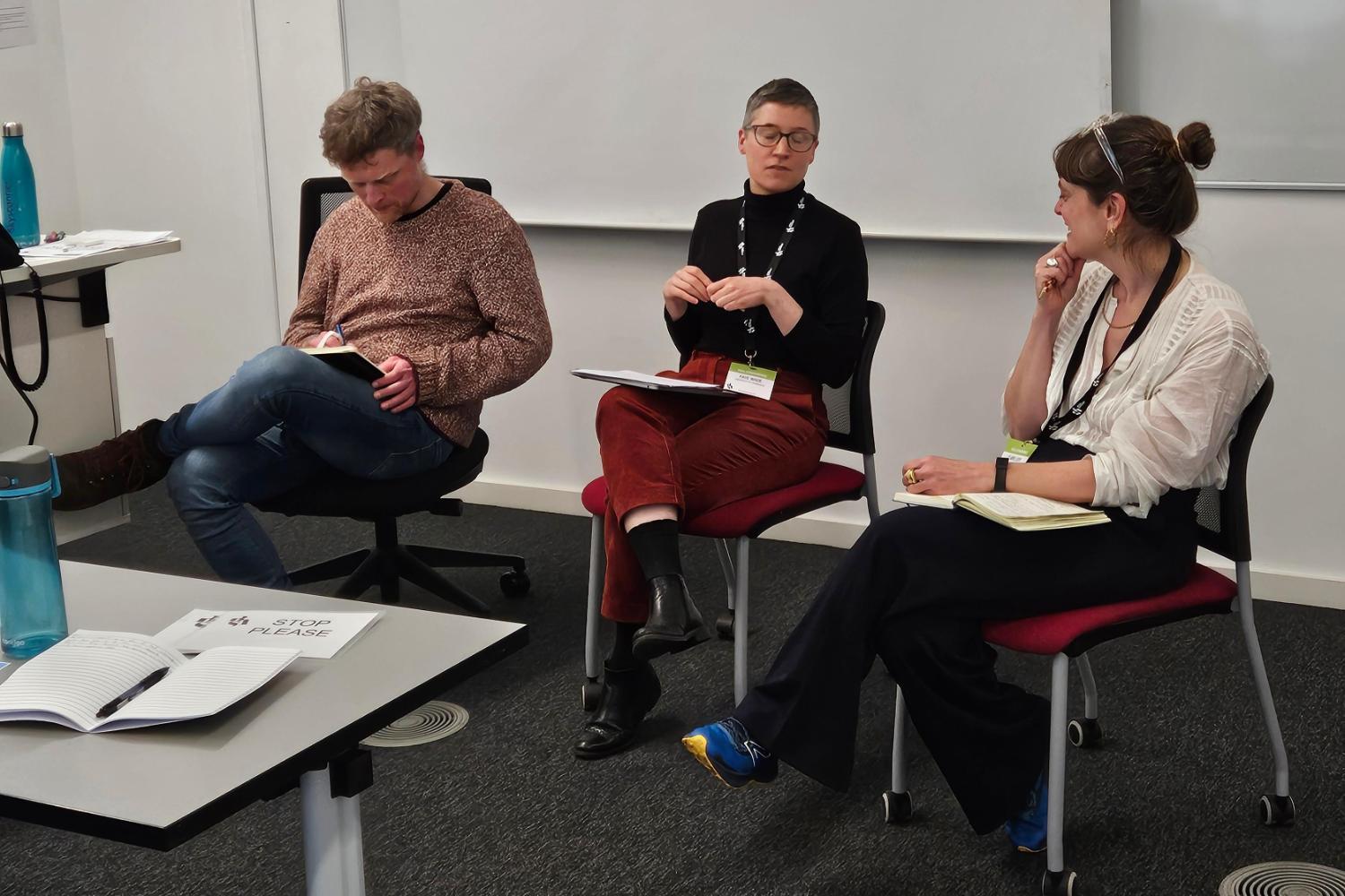 Three people sit on chairs at the front of a conference room
