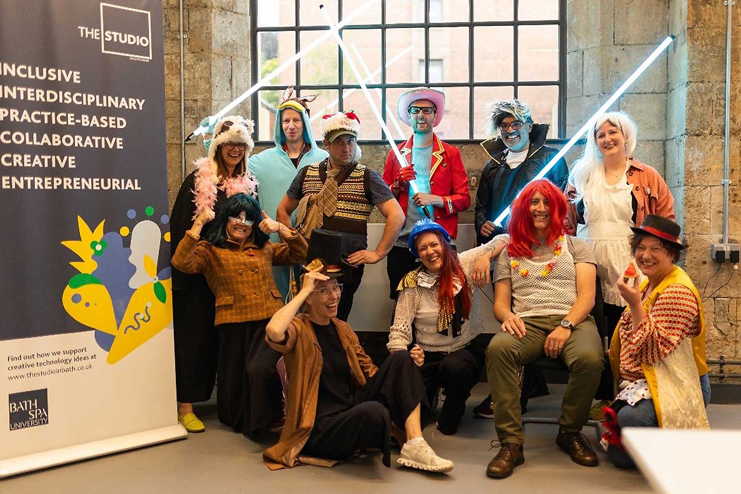 A group of people in fancy dress pose next to a promotional banner for The Studio