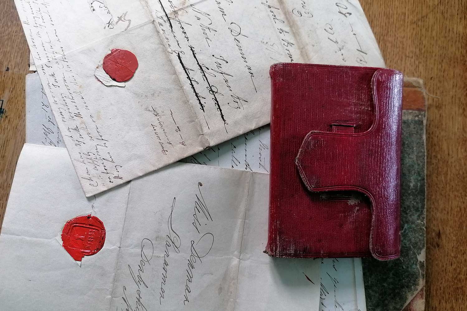 A leatherbound burgundy diary sits atop a pile of handwritten letters with red wax seals